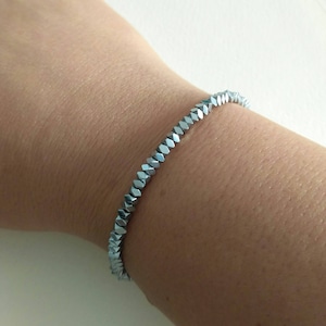 May include: A silver bracelet made of faceted beads. The bracelet is worn on a person's wrist.