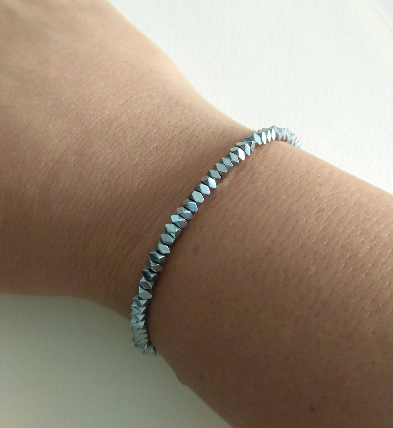 May include: A silver bracelet made of faceted beads. The bracelet is worn on a person's wrist.