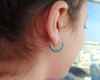 Puede incluir: Aretes de aro de oro con cuentas de piedras preciosas azules. Los aretes son pequeños y delicados.