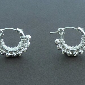 May include: A pair of silver hoop earrings with small silver beads attached to the hoop. The earrings are made of wire and have a delicate, handcrafted look.