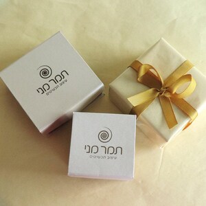 May include: Two white gift boxes with a gold ribbon and a gold swirl logo. The logo says "חנות מנו" which translates to "Mano Store" in English.