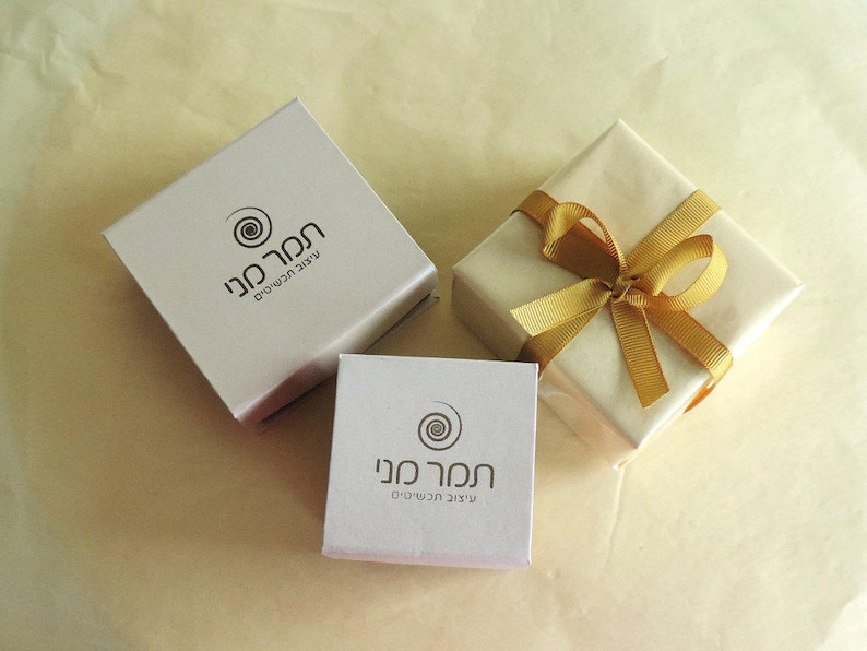 May include: Two white gift boxes with a gold ribbon and a gold swirl logo. The logo says "חנות מנו" which translates to "Mano Store" in English.