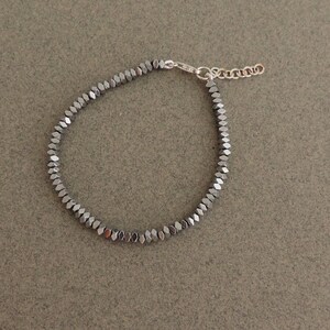 May include: A silver bracelet with a chain closure and a row of small, dark gray, faceted beads.