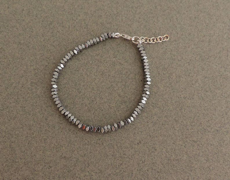May include: A silver bracelet with a chain closure and a row of small, dark gray, faceted beads.