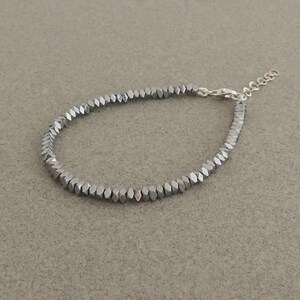 May include: A silver bracelet made of small, faceted, hexagonal beads.