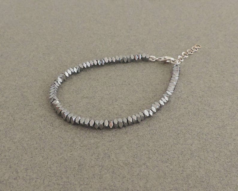 May include: A silver bracelet made of small, faceted, hexagonal beads.