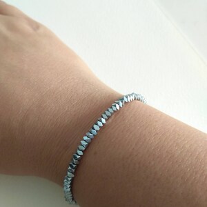 May include: A silver bracelet made of faceted beads. The bracelet is on a person's wrist.