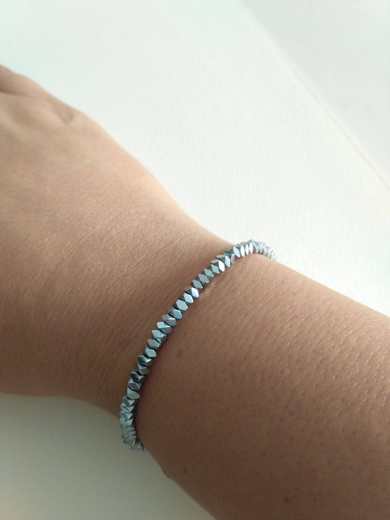 May include: A silver bracelet made of faceted beads. The bracelet is on a person's wrist.