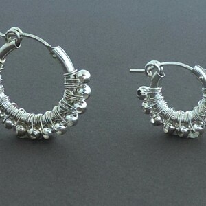 May include: A pair of silver hoop earrings with small beads woven into the wire. The earrings are simple and elegant.