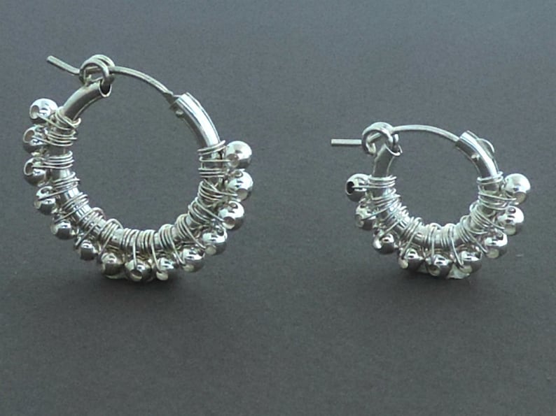 May include: A pair of silver hoop earrings with small beads woven into the wire. The earrings are simple and elegant.