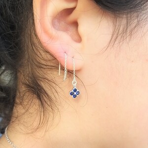 May include: A silver chain earring with a small blue gemstone cluster pendant. The earring is hanging from a person's earlobe.