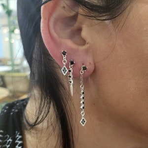 May include: Three silver earrings with black gemstones. The earrings are dangling and feature a diamond-shaped charm at the bottom.