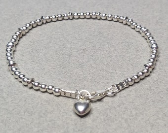 Pode incluir: Um bracelete de prata com contas e um fecho em forma de coração. O bracelete é feito de contas pequenas e redondas e tem um design simples e elegante.