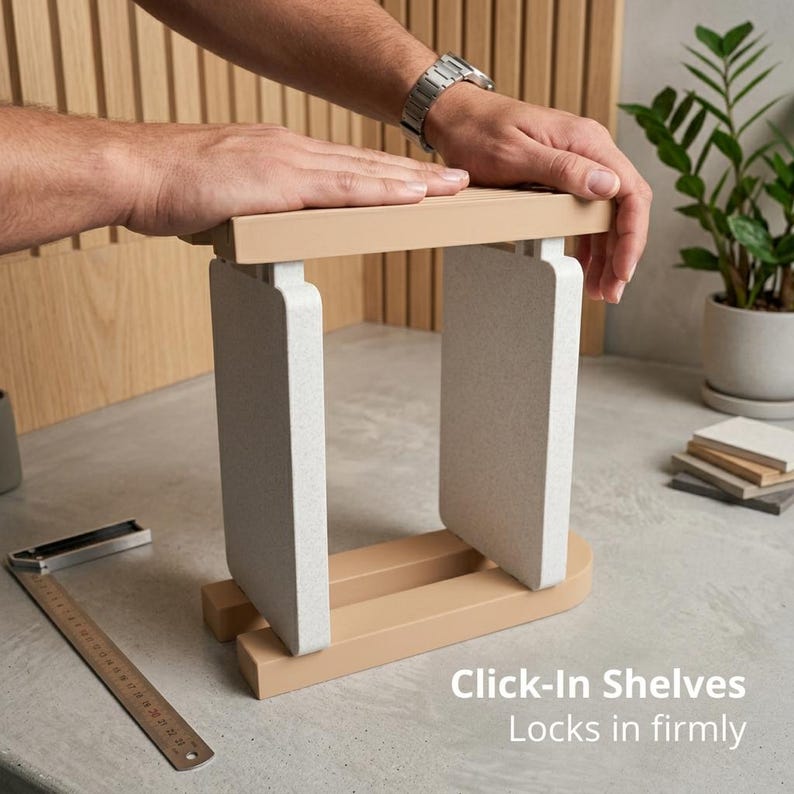 May include: A modular shelving unit featuring two light beige horizontal bars and two vertical speckled white panels. The structure is designed with a click-in mechanism. A metal ruler is visible on the surface, and the text reads: Click-In Shelves Locks in firmly.