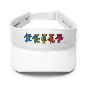 May include: A white visor featuring an embroidered graphic of five dancing bears in blue, green, yellow, orange, and pink. The visor has a structured front panel and an adjustable strap at the back with the text 110 FLEXFIT printed on the inner band.