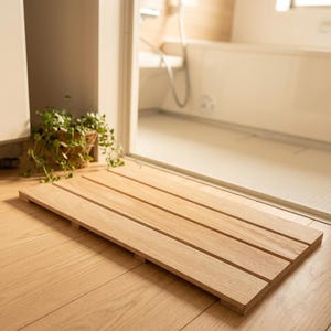 Op de afbeelding: Een rechthoekige badmat opgebouwd uit lichtgekleurde houten latten die horizontaal zijn gerangschikt. De mat heeft een natuurlijke houtnerfafwerking en wordt iets van de vloer getild door kleine steunbalken onder het lattenoppervlak.