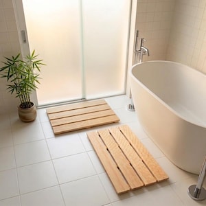 May include: Two rectangular wooden bath mats featuring a slatted design with visible grain patterns. The mats are constructed from light-toned wood planks arranged side-by-side with narrow gaps between each piece, providing a flat surface.