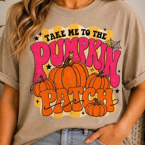 以下が含まれることがあります： 黒、ピンク、オレンジの文字で「TAKE ME TO THE PUMPKIN PATCH」と書かれたグラフィックプリントが施されたベージュの半袖Tシャツ。デザインには、4つのオレンジ色のカボチャ、黄色の縦縞、黒い星、クモの巣が含まれています。