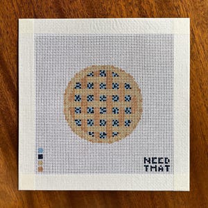 May include: A square needlepoint canvas featuring a circular lattice-crust pie design with blue berry filling. The canvas includes a color palette guide on the left and the text "NEED THAT" in the bottom right corner, all on a white grid.