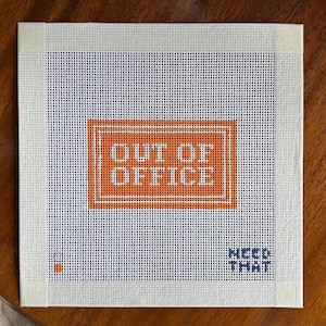 May include: A square needlepoint canvas featuring a white grid background with a central orange rectangular border containing the text OUT OF OFFICE in white. The bottom right corner displays the text NEED THAT in dark blue, with a small orange square.