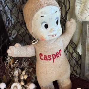 May include: A vintage Casper the Friendly Ghost doll featuring a white molded plastic face with painted facial features, a tan terry cloth body, and the name Casper embroidered in red thread on the chest. The doll has outstretched arms.