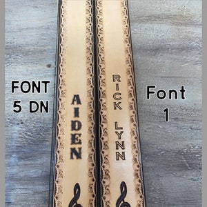 Pu&ograve; includere: Due cinturini in pelle con cuciture decorative e un design a nota musicale. I cinturini sono personalizzati con i nomi "Aiden" e "Rick Lynn" in diversi caratteri. Il testo "Font 5 DN" e "Font 1" &egrave; anche visibile.