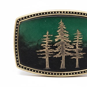 A decorative metal buckle with a green background and gold tree silhouettes.