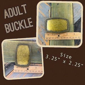 May include: A gold-toned metal belt buckle with a rectangular shape and a dotted border. The buckle measures 3.25 inches by 2.25 inches.