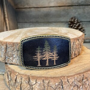 A black leather belt buckle with a tree design on it, placed on a wooden surface.