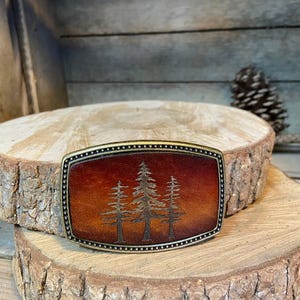 A wooden board with a decorative metal buckle featuring a tree design in the center.