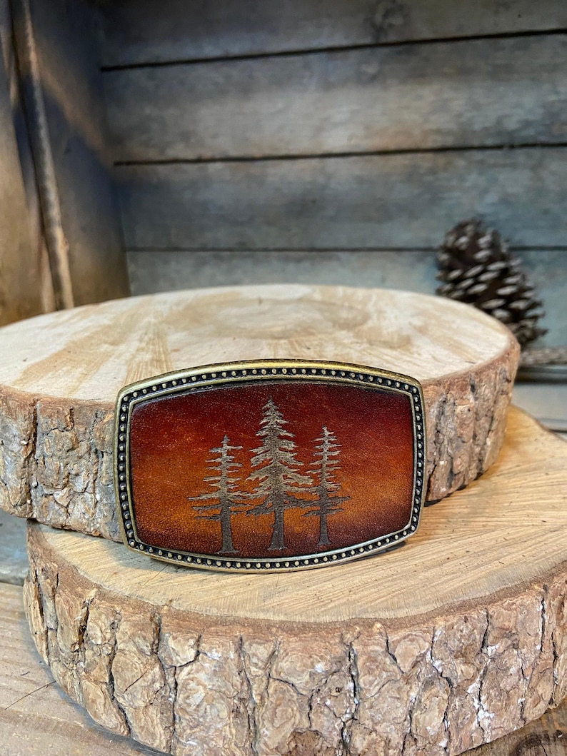 A wooden board with a decorative metal buckle featuring a tree design in the center.