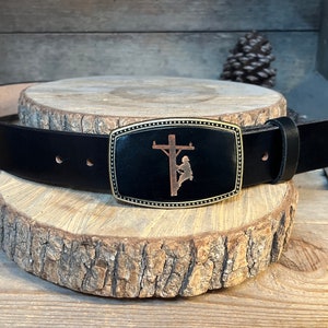May include: A black leather belt with a gold-toned buckle featuring a silhouette of a lineman working on a power pole.