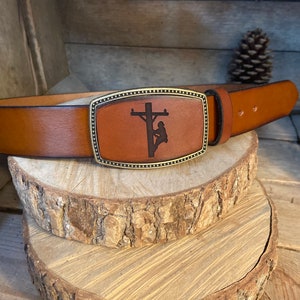 May include: A brown leather belt with a brass buckle featuring a silhouette of a lineman working on a power pole.