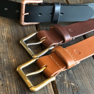 May include: Three leather belts with different colored buckles. The top belt is black with a copper buckle. The middle belt is brown with a silver buckle. The bottom belt is tan with a brass buckle.