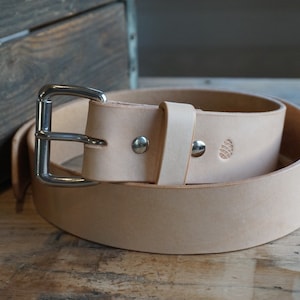 K&ouml;nnte beinhalten: Ein hellbrauner Lederg&uuml;rtel mit einer silbernen Schnalle. Der G&uuml;rtel hat ein kleines, gepr&auml;gtes Design auf dem Leder.