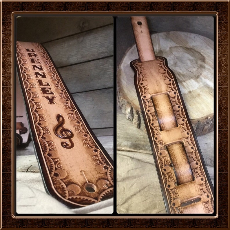 Pu&ograve; includere: Un cinturino per chitarra in pelle marrone chiaro con un motivo floreale decorativo e il nome "BRENLEY" in rilievo. Una chiave di violino &egrave; anche in rilievo sul cinturino.