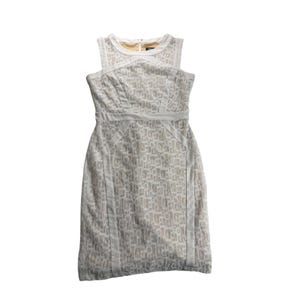 May include: A sleeveless knee-length dress featuring a white lace overlay with a geometric pattern over a solid beige lining. The dress has a round neckline, structured paneling along the bodice and waist, and a concealed zipper at the back neck.