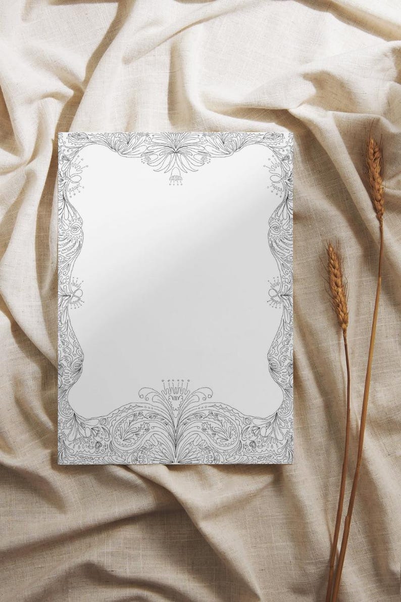 May include: A rectangular, white paper with an ornate black and white floral border. The design features detailed patterns of leaves, swirls, and floral elements. The paper is set against a neutral-toned fabric background, with two stalks of wheat.