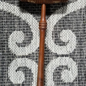 May include: A wooden gavel with a brown handle and a round head. The head is decorated with white lettering that reads "J.A.M."