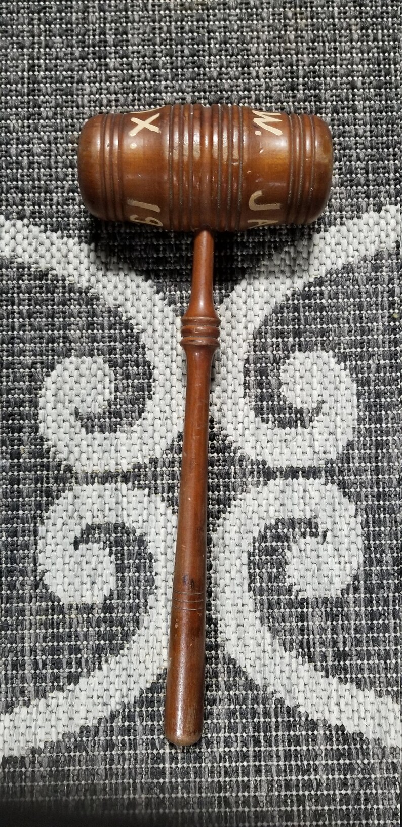 May include: A wooden gavel with a brown handle and a round head. The head is decorated with white lettering that reads "J.A.M."