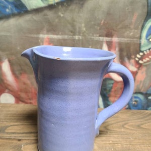 May include: A light blue ceramic pitcher with a handle. The pitcher has a slightly textured surface.