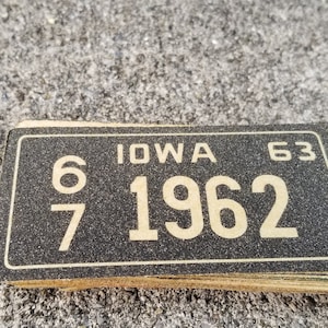 May include: A black and yellow vintage license plate with the text "IOWA 63" and the number "1962" printed on it.
