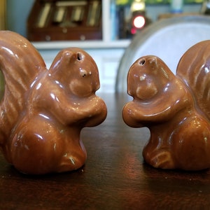 May include: A pair of brown ceramic squirrel salt and pepper shakers. The squirrels are facing each other and have their tails curled up.