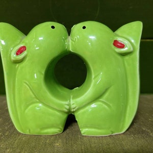 May include: A pair of green ceramic squirrel salt and pepper shakers. The squirrels are kissing and have red accents on their ears.