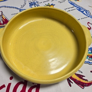 May include: A yellow ceramic baking dish with two handles. The dish has a crazed glaze and is slightly worn.