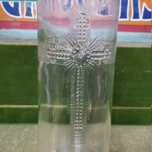 May include: A clear glass jar with a cross design embossed on the front. The jar is empty and has a wide mouth.