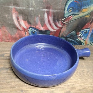 May include: A deep blue ceramic serving bowl with a single handle. The bowl has a smooth, slightly textured surface.