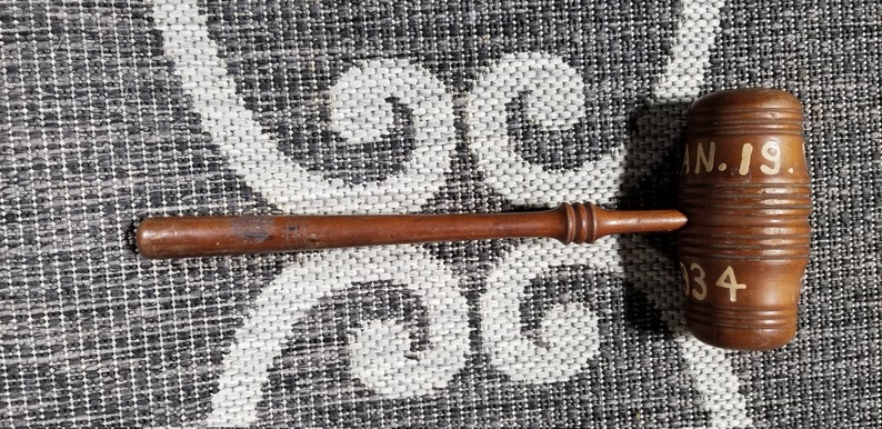 May include: A wooden gavel with a brown handle and a rectangular head. The head is engraved with the text "JAN. 19. 34".