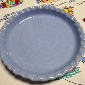 May include: A light blue pie plate with a scalloped edge. The plate is made of ceramic and has a speckled finish.