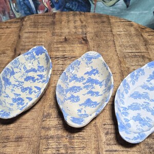 May include: Four ceramic leaf-shaped dishes with a blue and white pattern are arranged on a wooden table. The dishes have a light blue and white design, and the table has a rustic, weathered appearance.